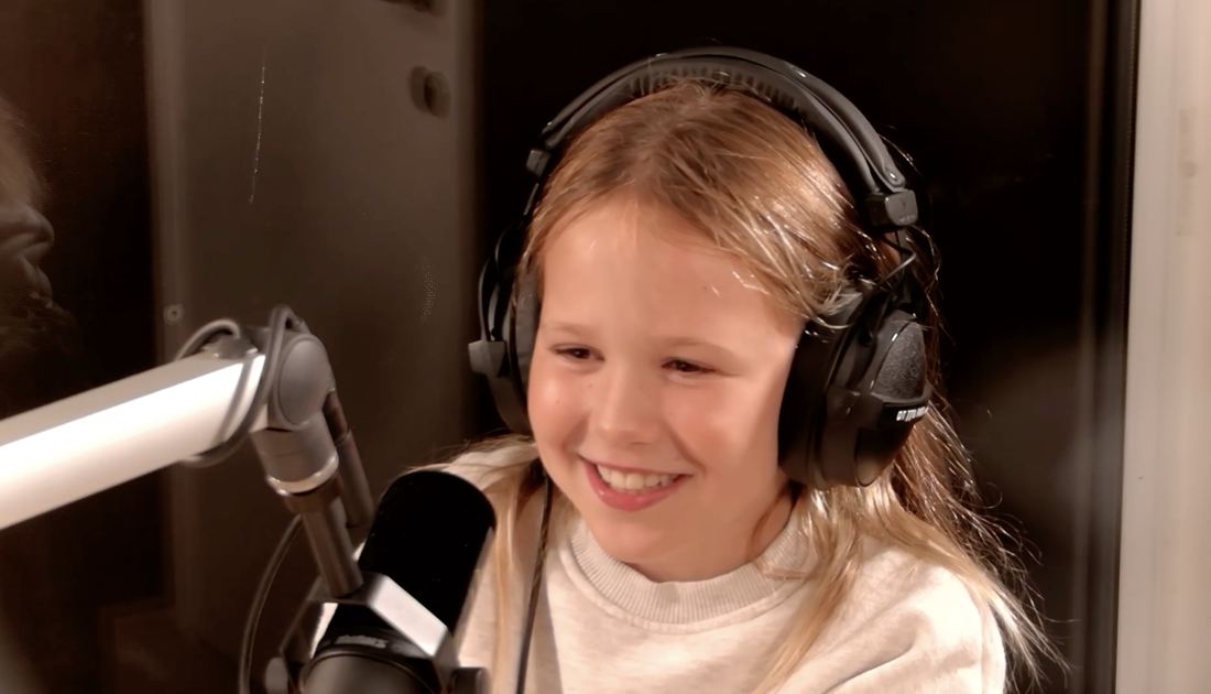 Juliette lacht met koptelefoon op aan de micro in de podcaststudio